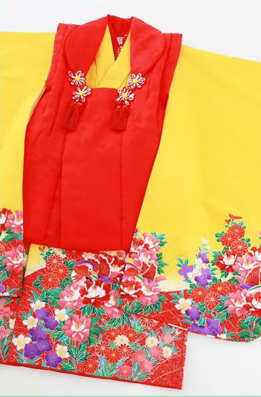 濃い黄色のお着物と赤い被布の組み合わせ。色とりどりの花模様が、袂と裾に施されています。
